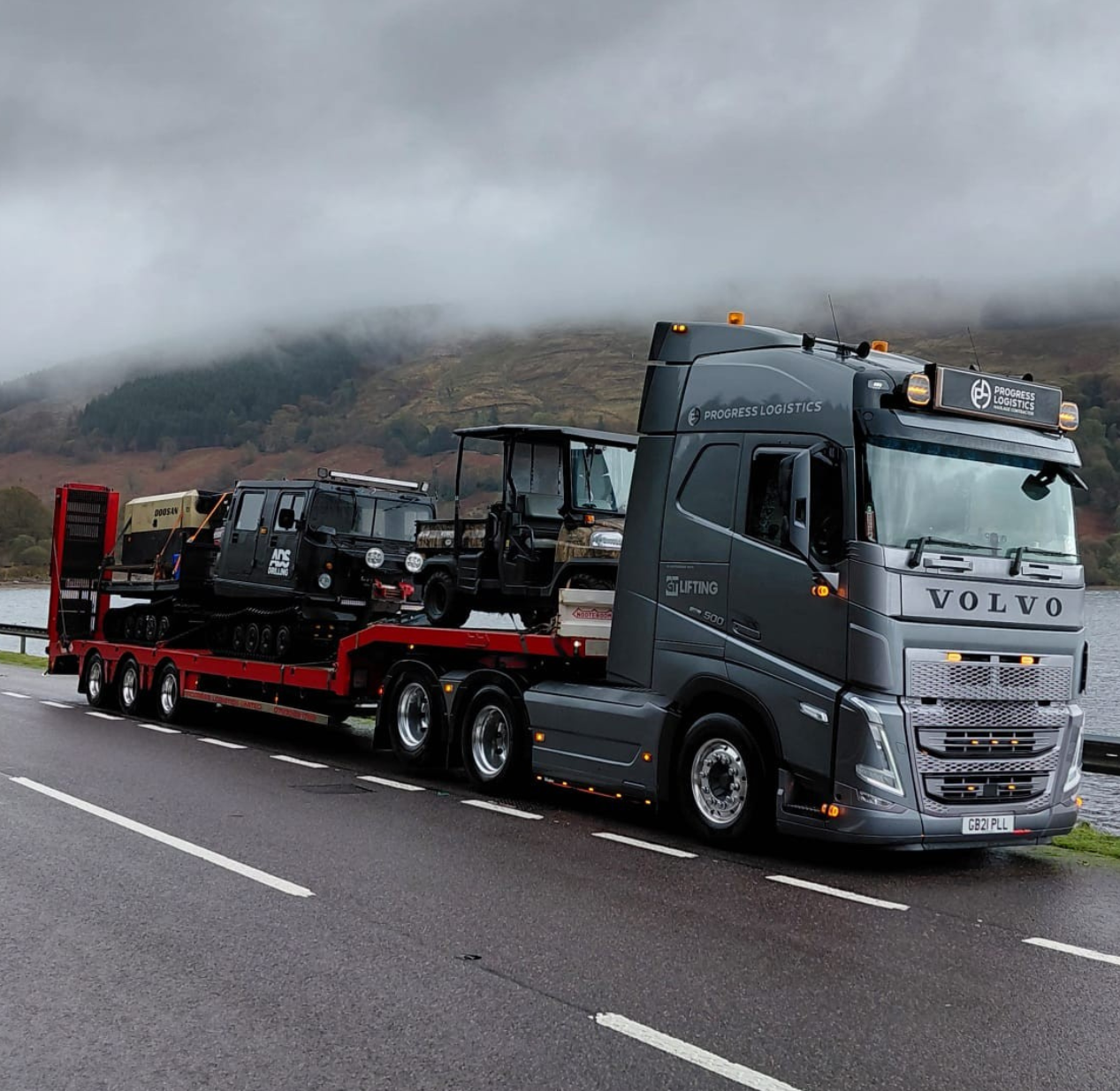 PRO 12 Progress Logistics Truck transporting machinery through a scenic mountain terrain